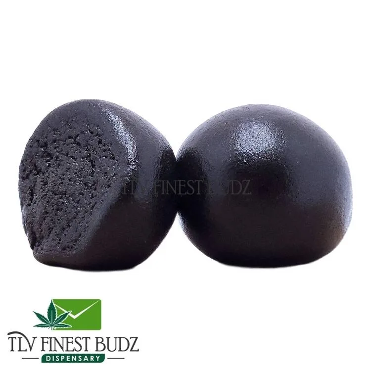 Two glossy black pakistani hash pieces, cut in half to reveal a dense interior, with a logo for TLV Finest Budz Dispensary at the bottom.
